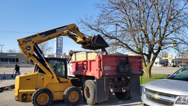 Bobcat dumping blacktop debris into a dump truck.