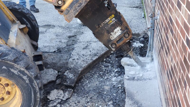 Jackhammer breaking up concrete by a building