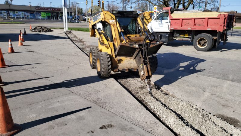 Bobcat with jackhammer digging a trench.