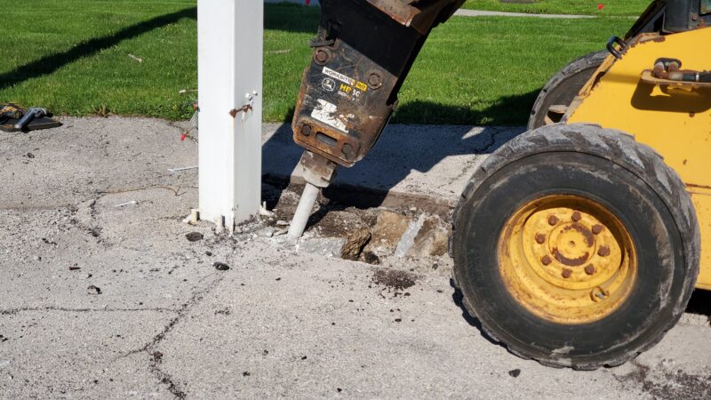 Jackhammer breaking up concrete by a sign.