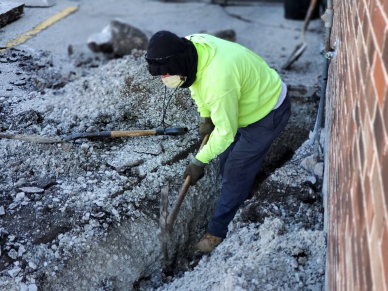 Construction worker digging a trench with a pick axe.