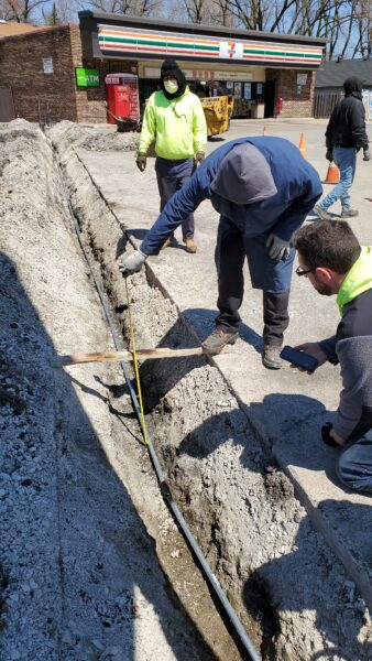 Electricians checking the depth of a trench.